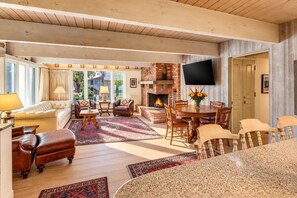 A spacious living room with a fireplace, a dining area, and a TV mounted on the wall.