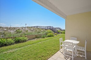 A patio with a table and chairs, a wooden deck, and a view of the beach.