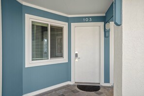 A front door with a number '103' above it, a window with blinds, and a doormat.