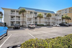 A multi-story hotel with a parking lot, featuring a central staircase, balconies, and palm trees.