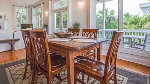 A dining area with a wooden table and chairs, large windows, and a view of greenery outside. - Baywatch | Steps to the Sand, Game Room, Bay View (Tybee Island)