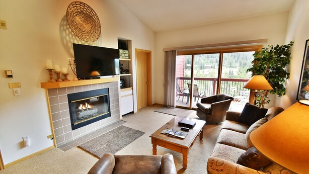A living room with a fireplace, a television, a sofa, and a balcony with outdoor furniture. - On River Trail! 2 Hot Tubs. Walk to Festivals, Dining, Shops, Activities (Keystone)