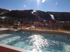 A hot tub with a view of a snowy mountain and a forest.