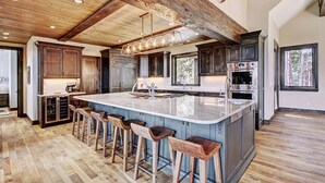 Una cocina amplia con una isla grande, taburetes de madera y techo rústico.