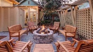 A fire pit surrounded by wooden chairs and tables in an outdoor patio area. - The WaterColor Escape You've Been Dreaming Of – Remodeled Kitchen/Golf Cart (Santa Rosa Beach)