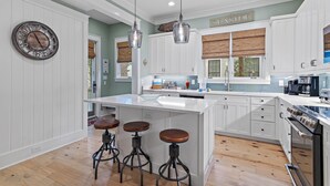 A modern kitchen with white cabinetry, a central island with stools, pendant lighting, and a clock on the wall. - The WaterColor Escape You've Been Dreaming Of – Remodeled Kitchen/Golf Cart (Santa Rosa Beach)