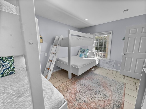 A bedroom with a bunk bed, a ladder, a small table, and a window.