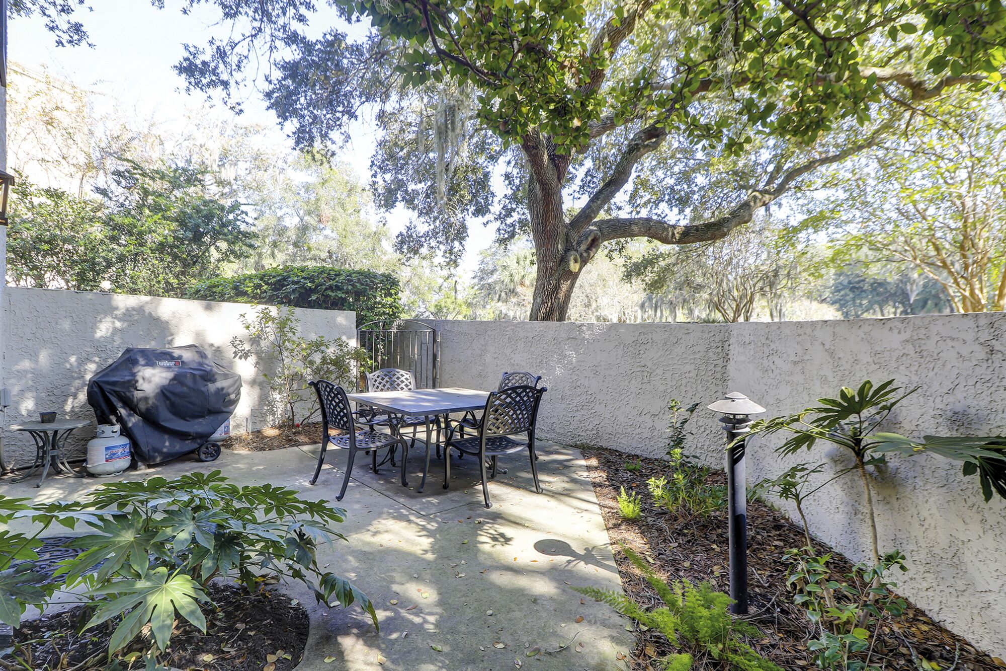 An outdoor patio with a table and chairs, a barbecue grill, and a gas cylinder.