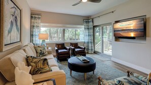 A spacious living room with a ceiling fan, a large TV, comfortable seating, and a view of the outdoors. - 433 Captains Walk- Completely Renovated - Oceanfront Villa in Palmetto Dunes! (Hilton Head Island)