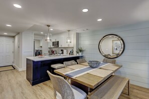A modern kitchen with white cabinets, a central island, and a dining area with a wooden table and wicker chairs.