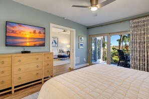 A bedroom with a large bed, a dresser, a television, and a view of the outdoors.