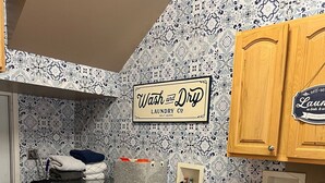 A laundry room with a washing machine, a sink, and a 'Wash and Dry Laundry Co.' sign.