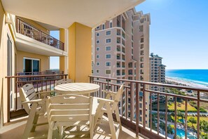 A balcony with a table and chairs, overlooking a beach and high-rise buildings.