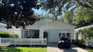 Une maison de plain-pied avec un garage, une clôture blanche en bois et un véhicule de golf garé devant.