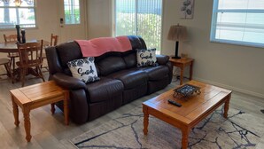 Un salon comprenant un canapé en cuir marron foncé, deux fauteuils assortis, une table basse en bois, un tapis et un coin repas avec une table et des chaises en bois.