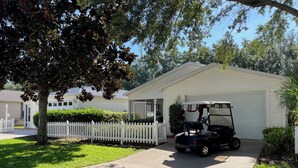 Une maison de plain-pied avec un garage, une clôture blanche en bois et un véhicule de golf garé devant.
