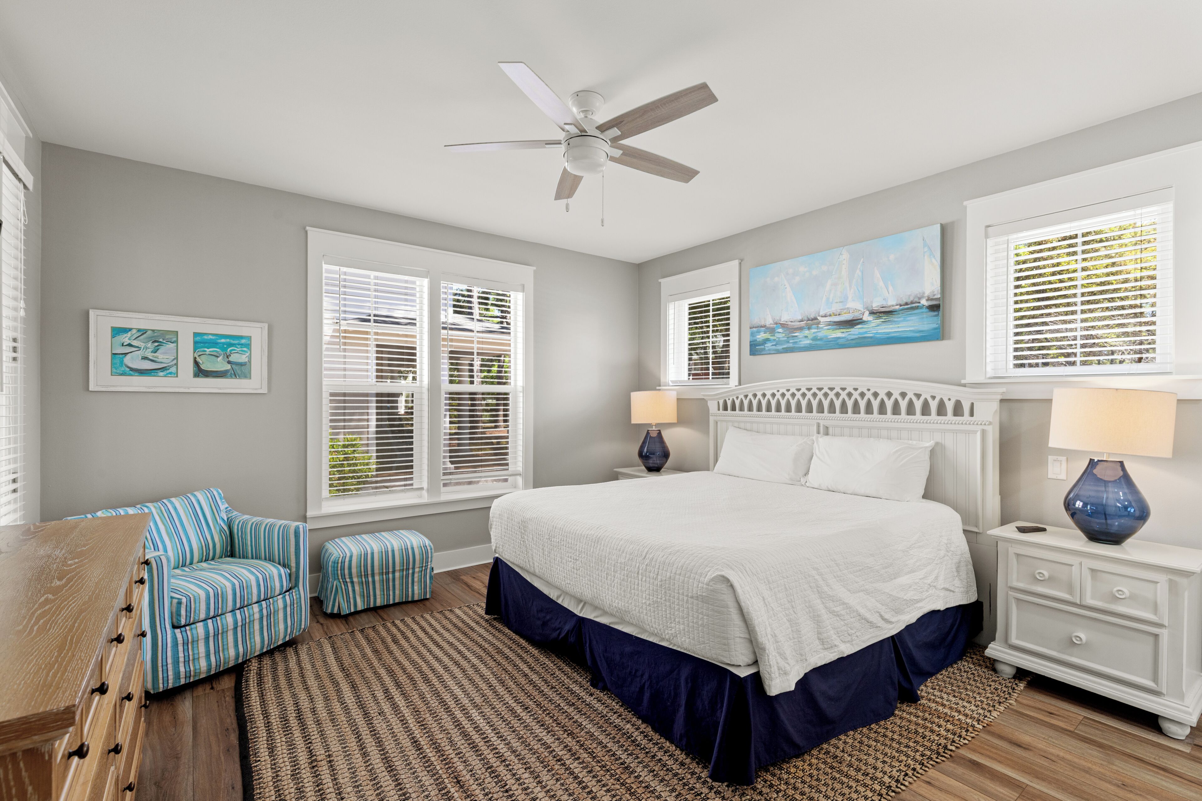 A bedroom with a bed, a chair, a nightstand, a lamp, and a ceiling fan.
