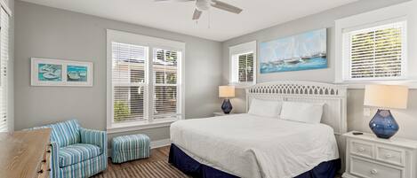 A bedroom with a bed, a chair, a nightstand, a lamp, and a ceiling fan.