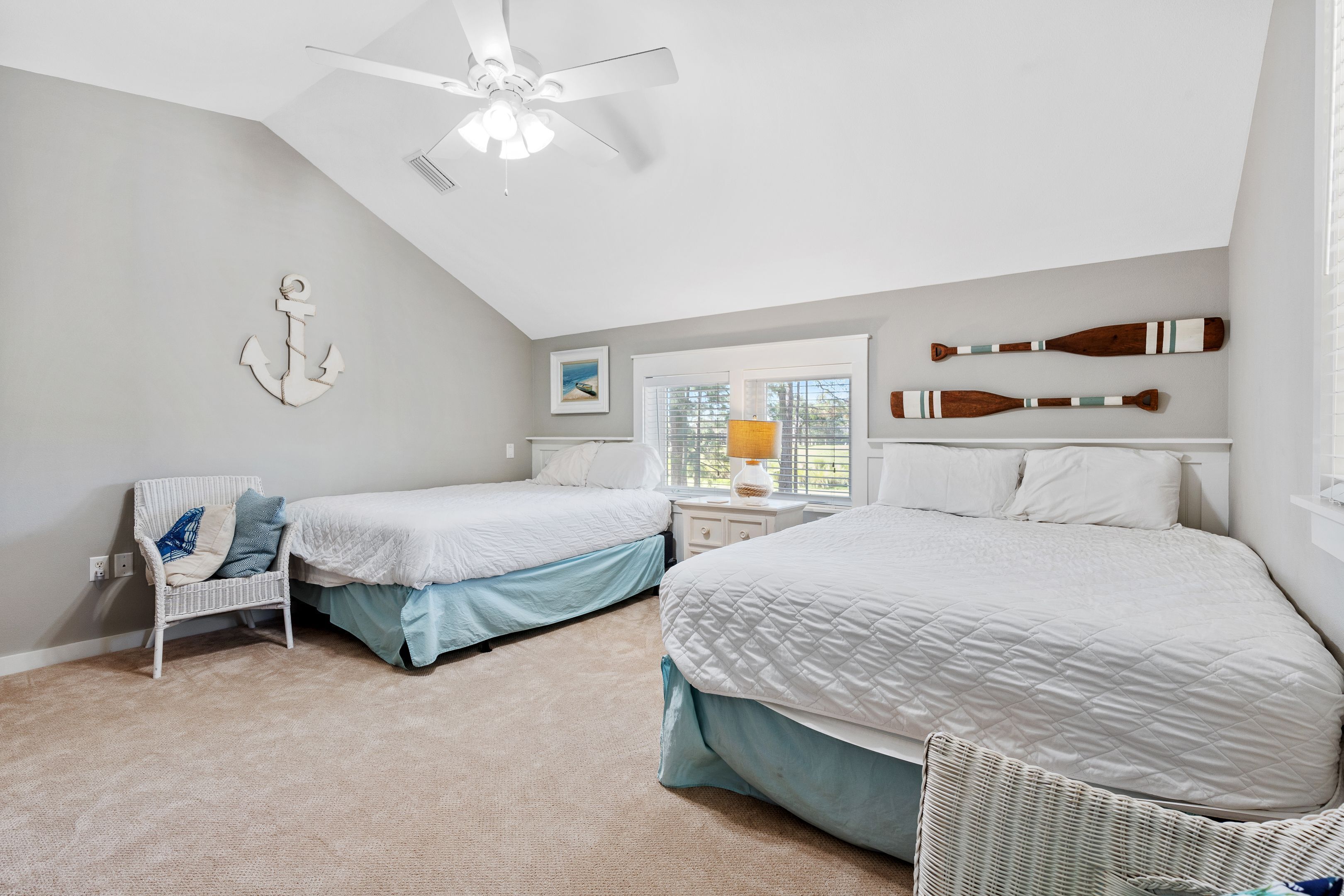A bedroom with two beds, a ceiling fan, a window with blinds, and a wall-mounted anchor decoration.
