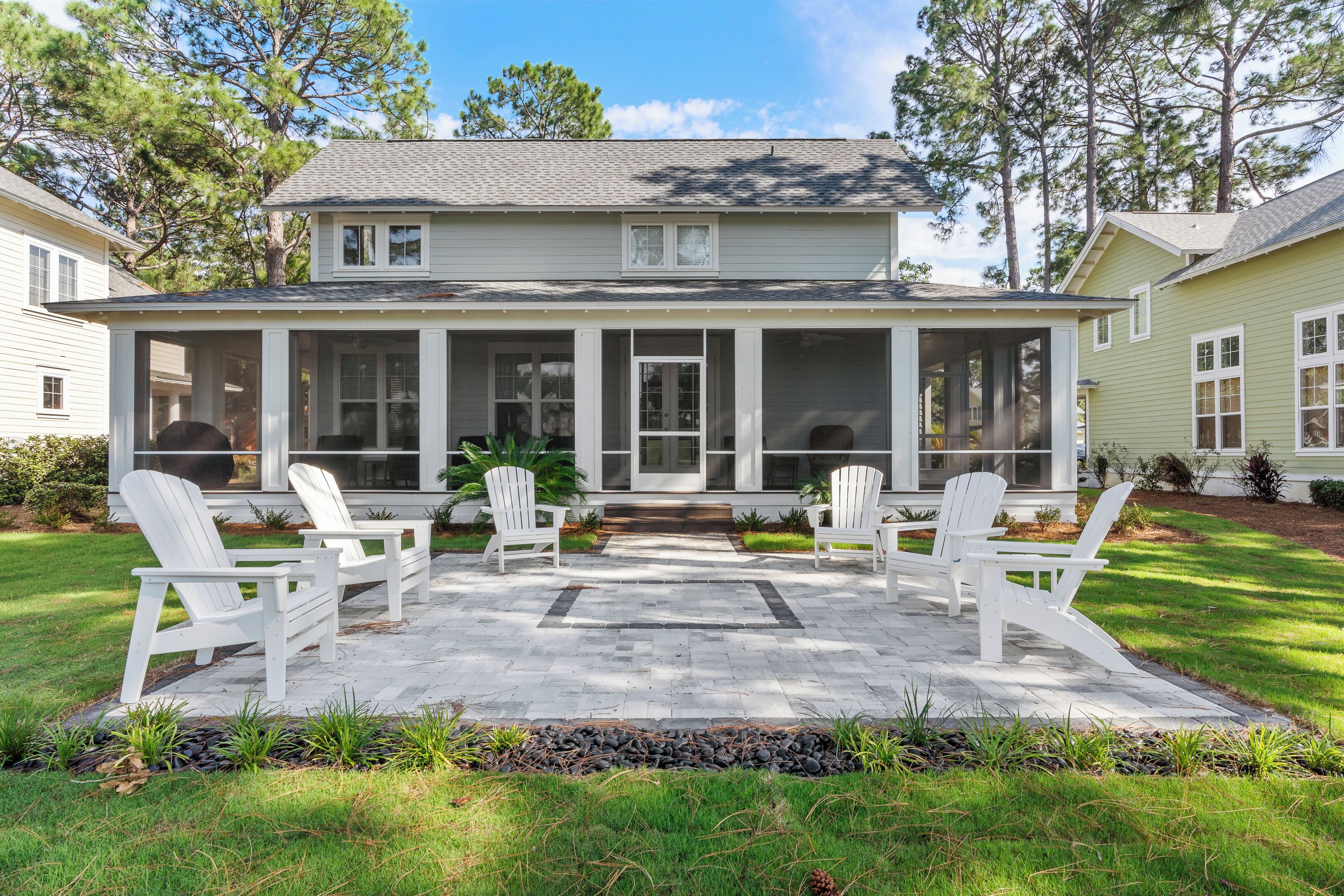 A two-story house with a covered porch, four white Adirondack chairs, and a stone pathway leading to the entrance.