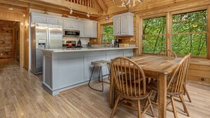 Interieur van een houten blokhut met keuken en eetgedeelte, met een groot eiland, houten stoelen en een kroonluchter.