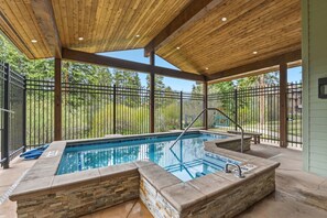 A covered outdoor swimming pool with stone walls, a wooden ceiling, and a metal fence.