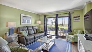 A living room with a leather sofa, a glass coffee table, and a view of a golf course through large windows.
