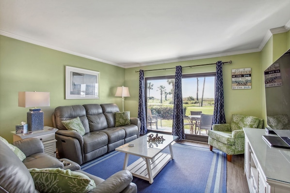 A living room with a leather sofa, a glass coffee table, and a view of a golf course through large windows.