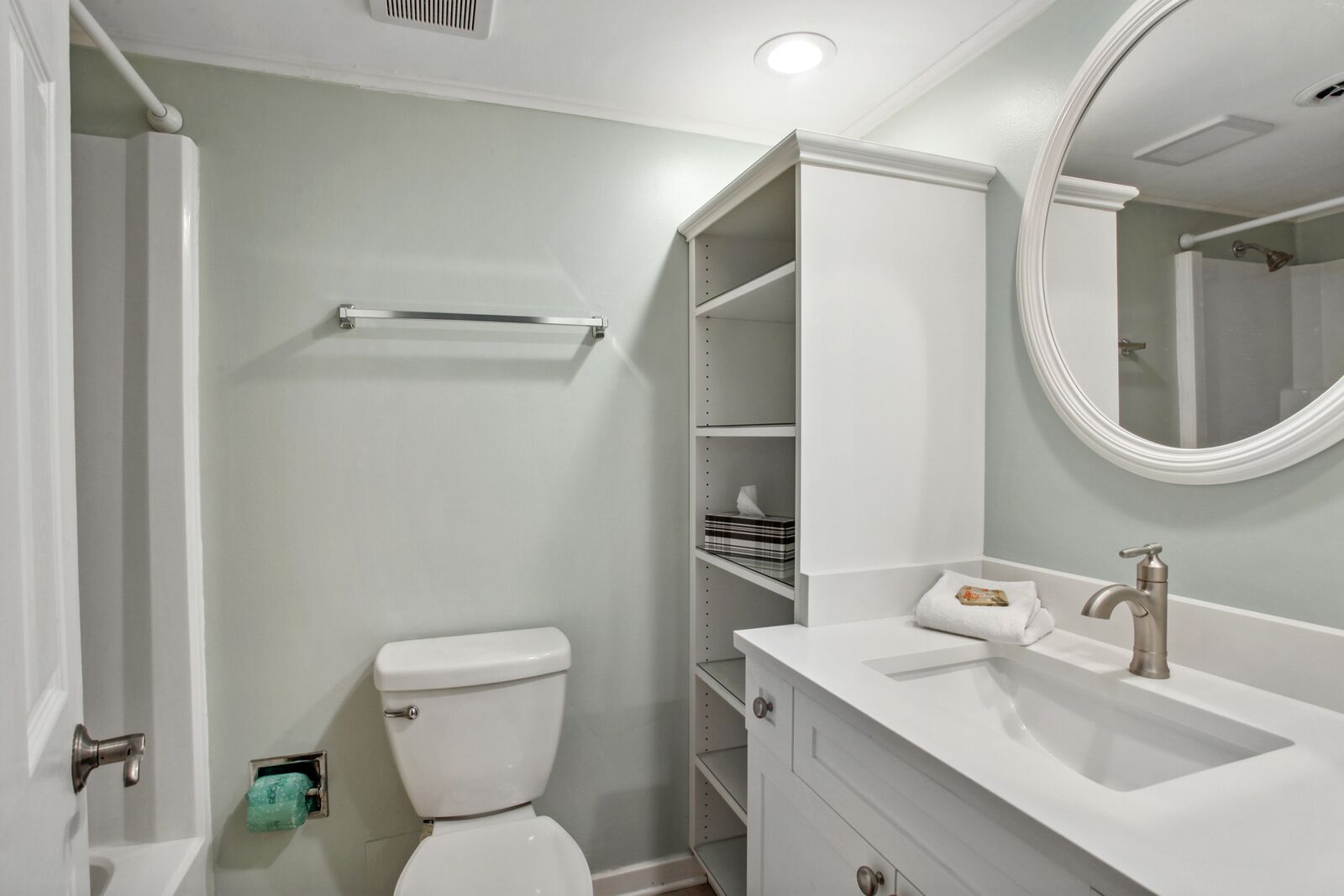 A bathroom with a toilet, a sink, a mirror, and built-in shelves.