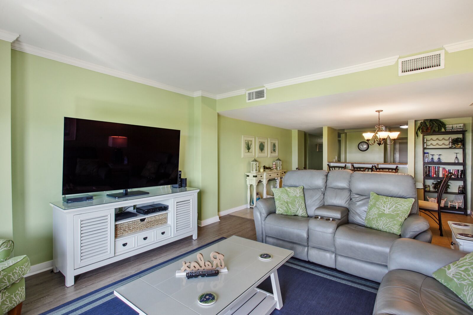 A living room with a flat-screen TV, leather sofa, and a bookshelf.