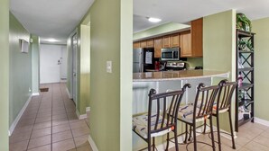 A kitchen with wooden cabinets, a microwave, and a refrigerator. There are two chairs with a patterned cushion.