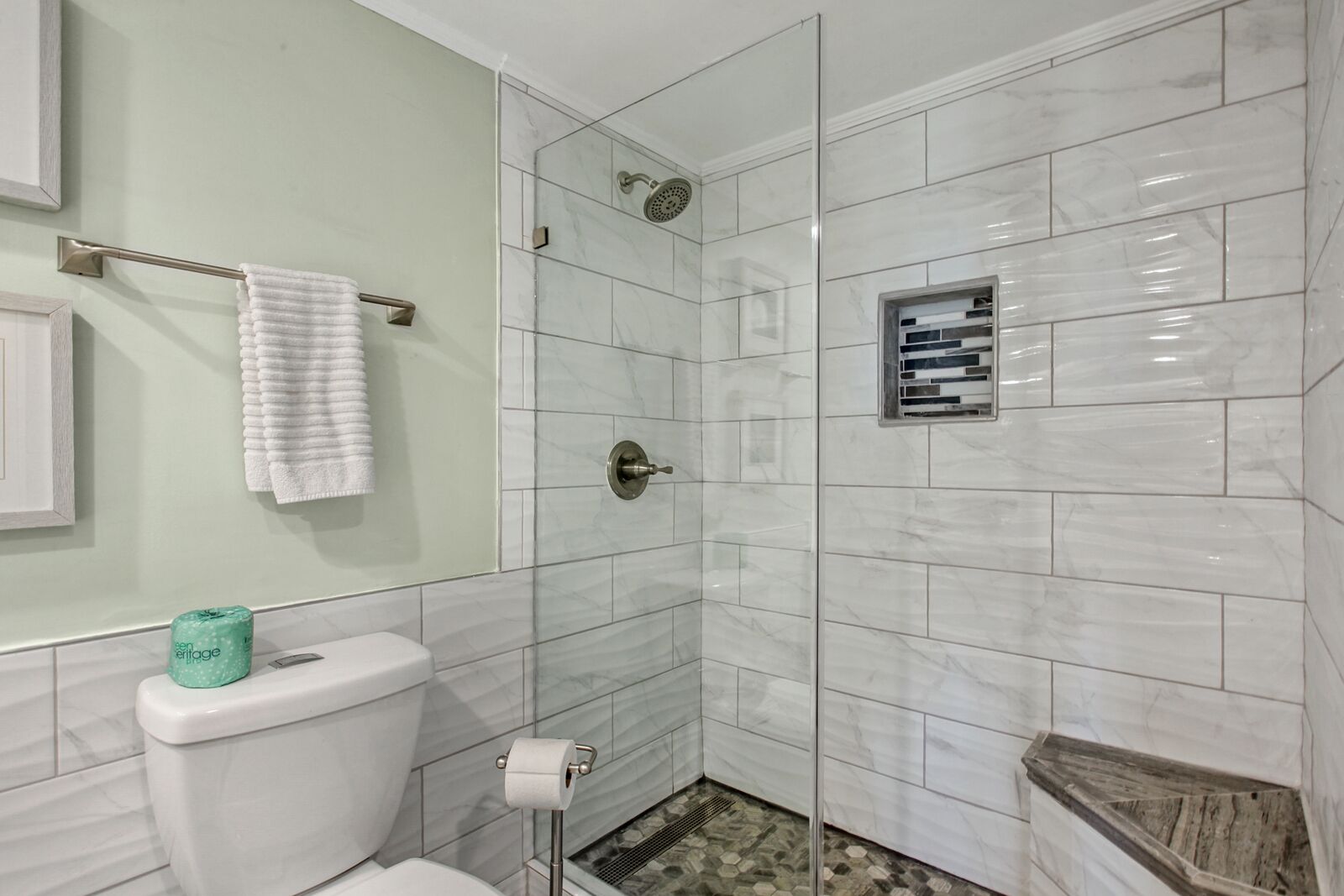 Une salle de bain comprenant des toilettes, une douche avec une porte en verre, un porte-serviettes et un support à papier toilette.