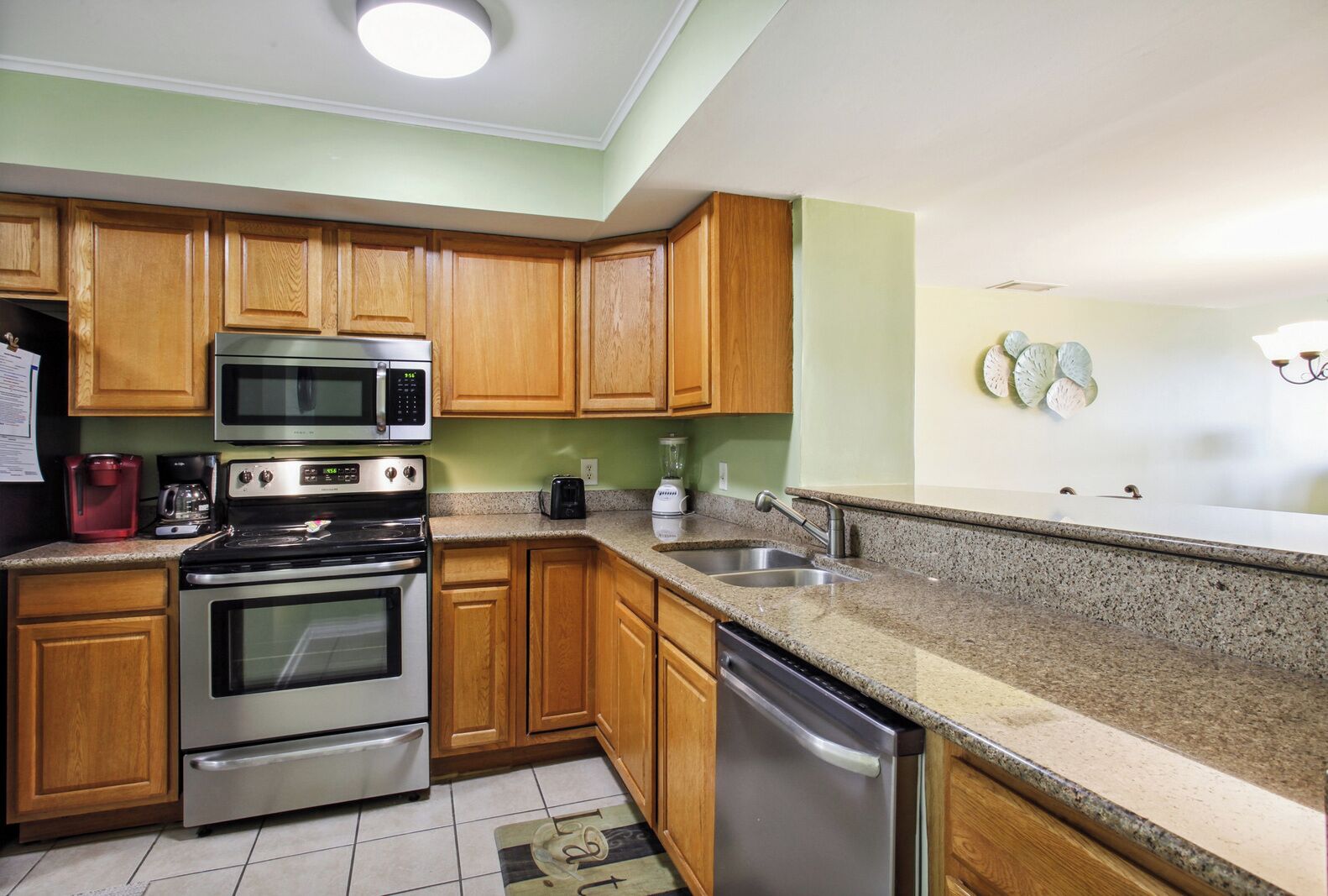 A kitchen with wooden cabinets, stainless steel appliances, granite countertops, and a tiled floor.