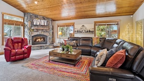 A cozy living room with a stone fireplace, leather furniture, and large windows.