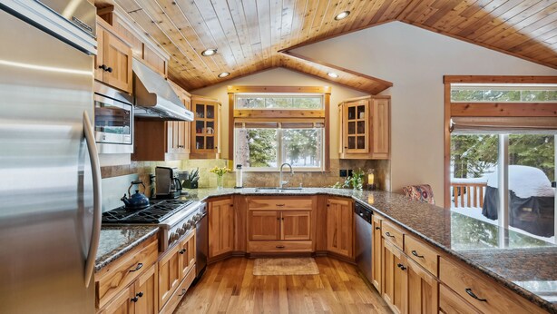 A modern kitchen with wooden cabinets, stainless steel appliances, and a large window providing a view of the outdoors.