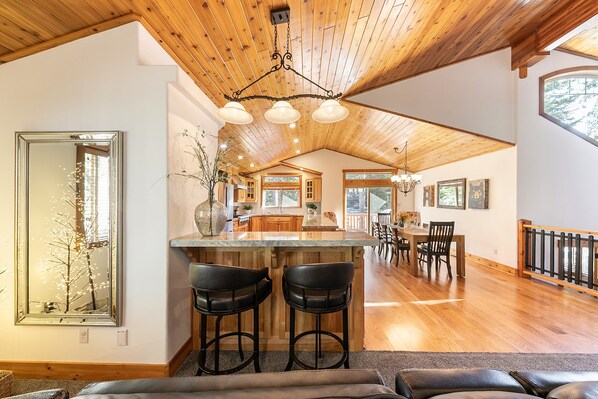 A spacious kitchen with a wooden ceiling, a large island with bar stools, and a dining area with a view of the outdoors.