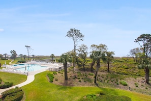 Uma área de piscina com espreguiçadeiras, um caminho e vegetação ao redor.