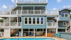 A two-story building with a pool, outdoor seating, and a staircase leading to a balcony. - ONLY 370 feet to beach access! HUGE LOADED home! Private Pool, Hot Tub, Game room with Pool Table! (Southern Shores)