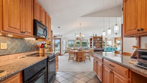 A spacious kitchen with wooden cabinets, a granite countertop, and a dining area with a chandelier. - ONLY 370 feet to beach access! HUGE LOADED home! Private Pool, Hot Tub, Game room with Pool Table! (Southern Shores)