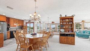 A spacious kitchen with wooden cabinets, a dining area with a large table and chairs, and a cozy living area with a blue sofa and a bookshelf. - ONLY 370 feet to beach access! HUGE LOADED home! Private Pool, Hot Tub, Game room with Pool Table! (Southern Shores)