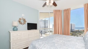 Een slaapkamer met een groot bed, een dressoir, een televisie en uitzicht op de stad en de oceaan vanuit het balkon.