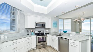 A modern kitchen with white cabinetry, stainless steel appliances, and a view of the city. - Updated Modern Beachfront Condo w/ Stunning Gulf Views in Destin! 🌴☀🌊 (Destin)
