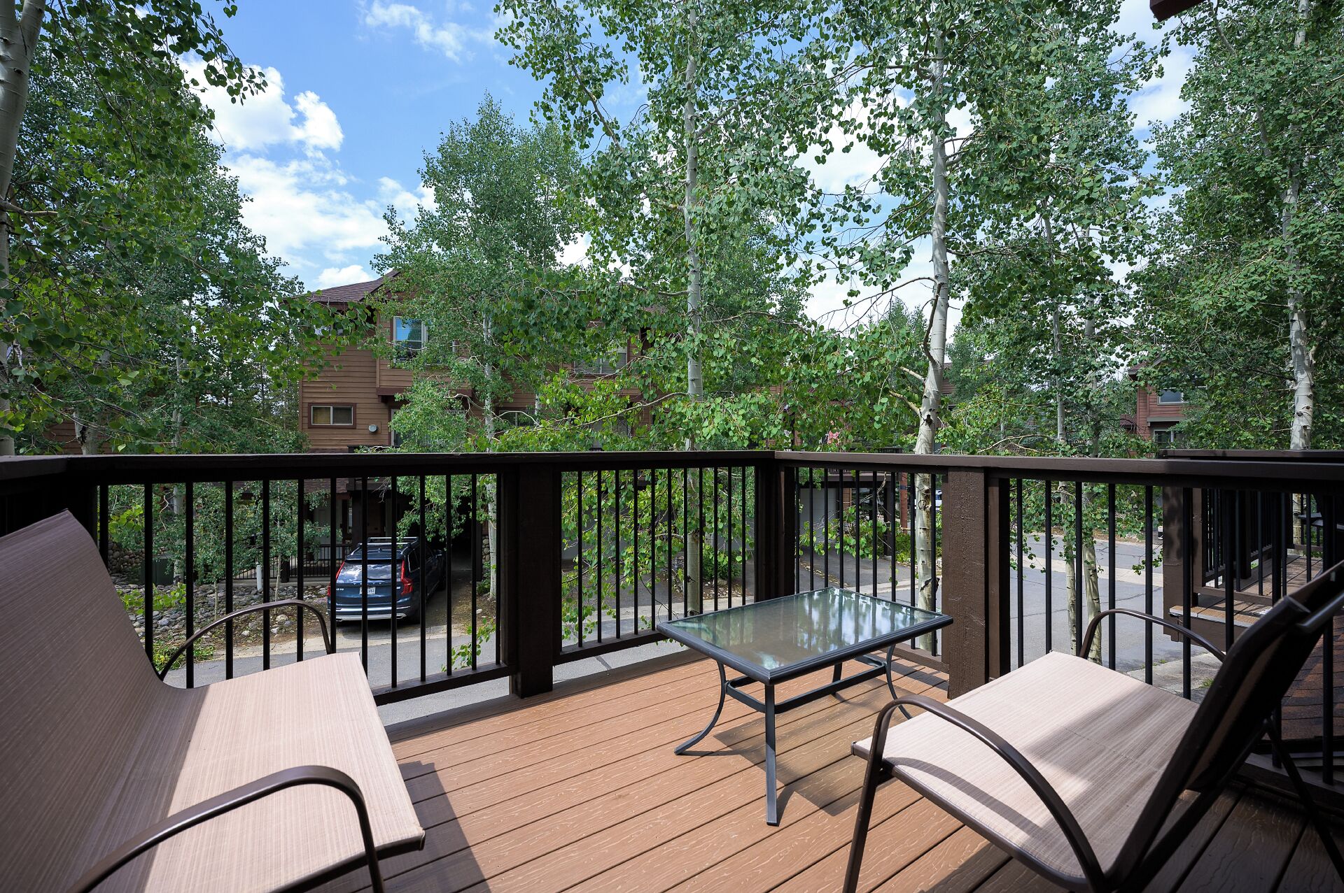 A wooden deck with a glass table and two chairs, surrounded by a metal railing.