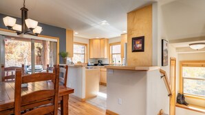 A modern kitchen with wooden cabinets, a central island, and a dining area with a wooden table and chairs. - Sawmill Station 220 | Private Hot Tub | Walk To Shops & Dining (Winter Park)