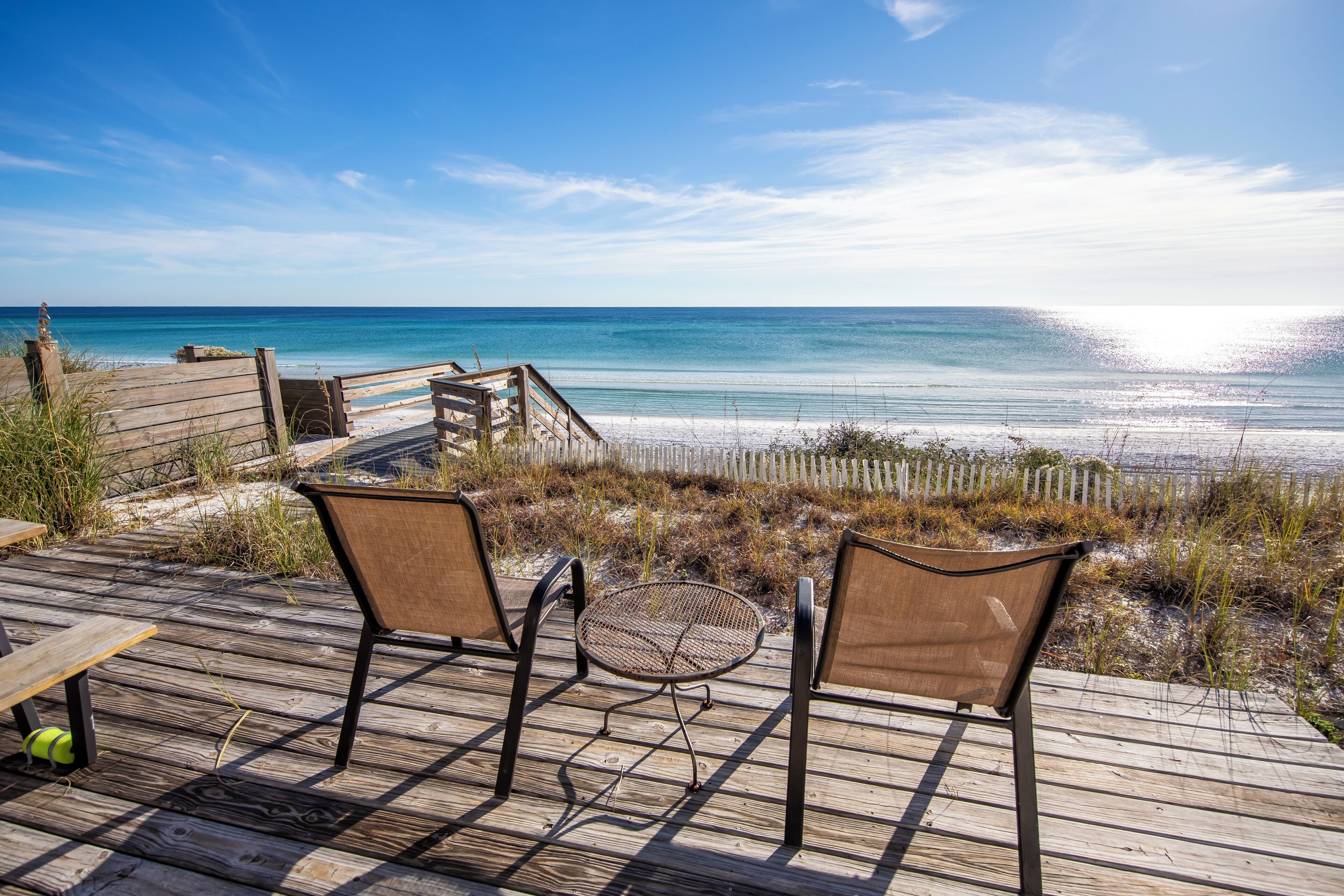A wooden deck with two chairs and a small table overlooking a beach.