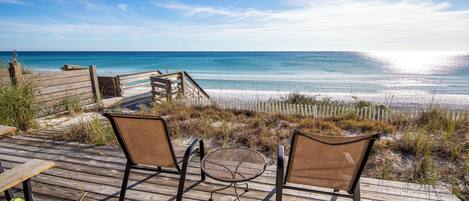 A wooden deck with two chairs and a small table overlooking a beach.