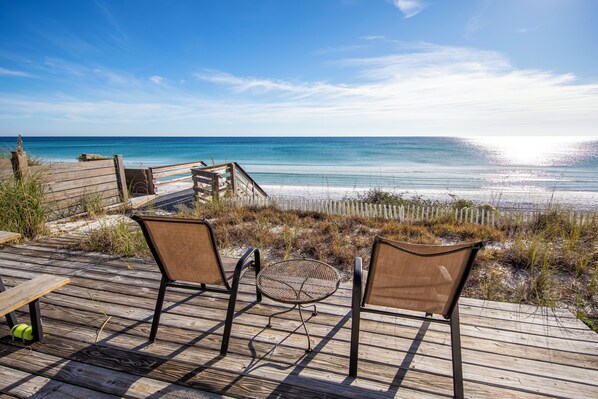A wooden deck with two chairs and a small table overlooking a beach.