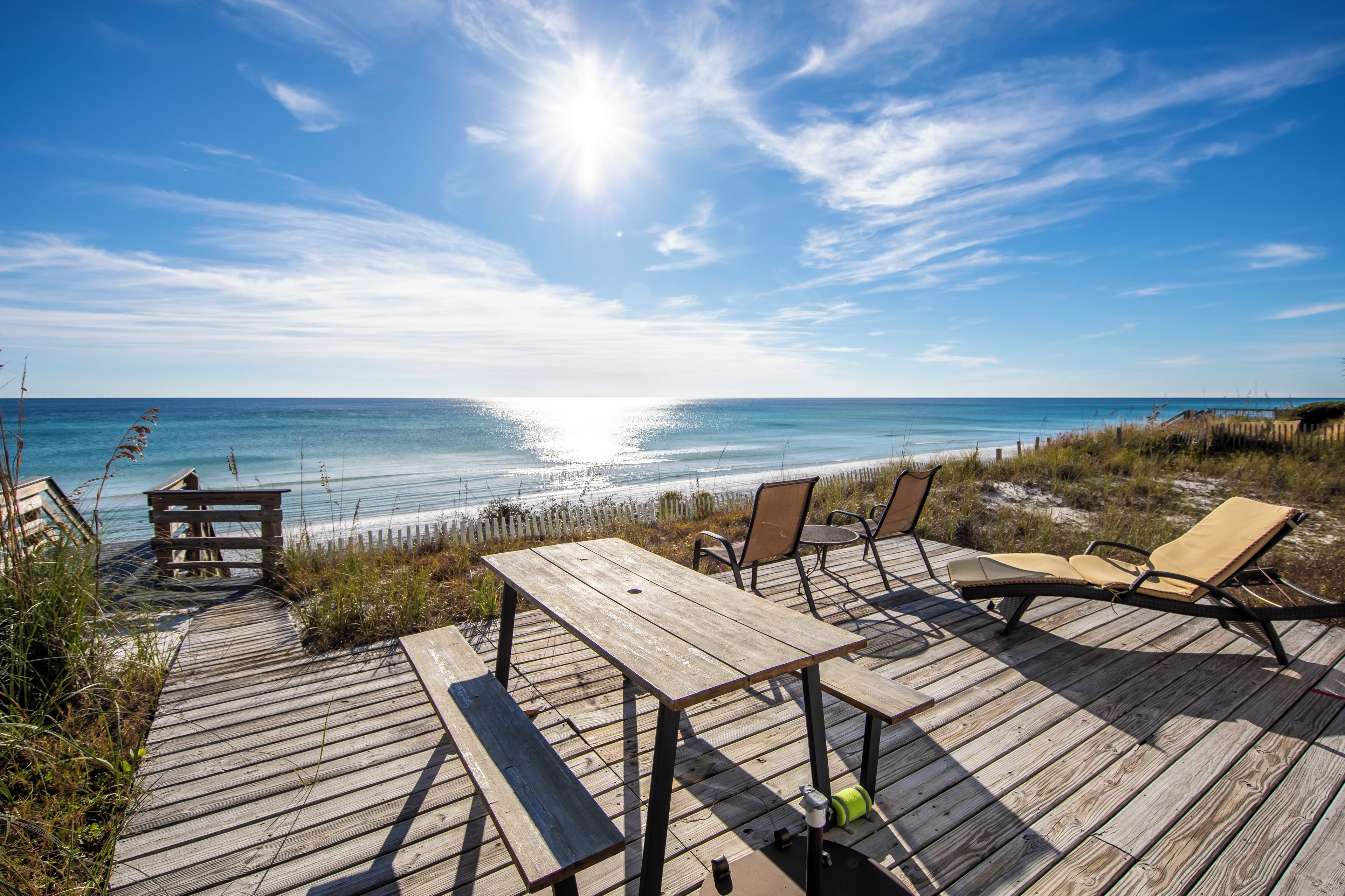 A wooden deck with a table and chairs overlooking a beach.