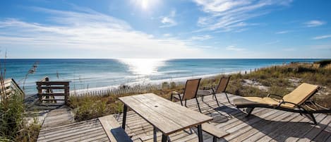 A wooden deck with a table and chairs overlooking a beach.