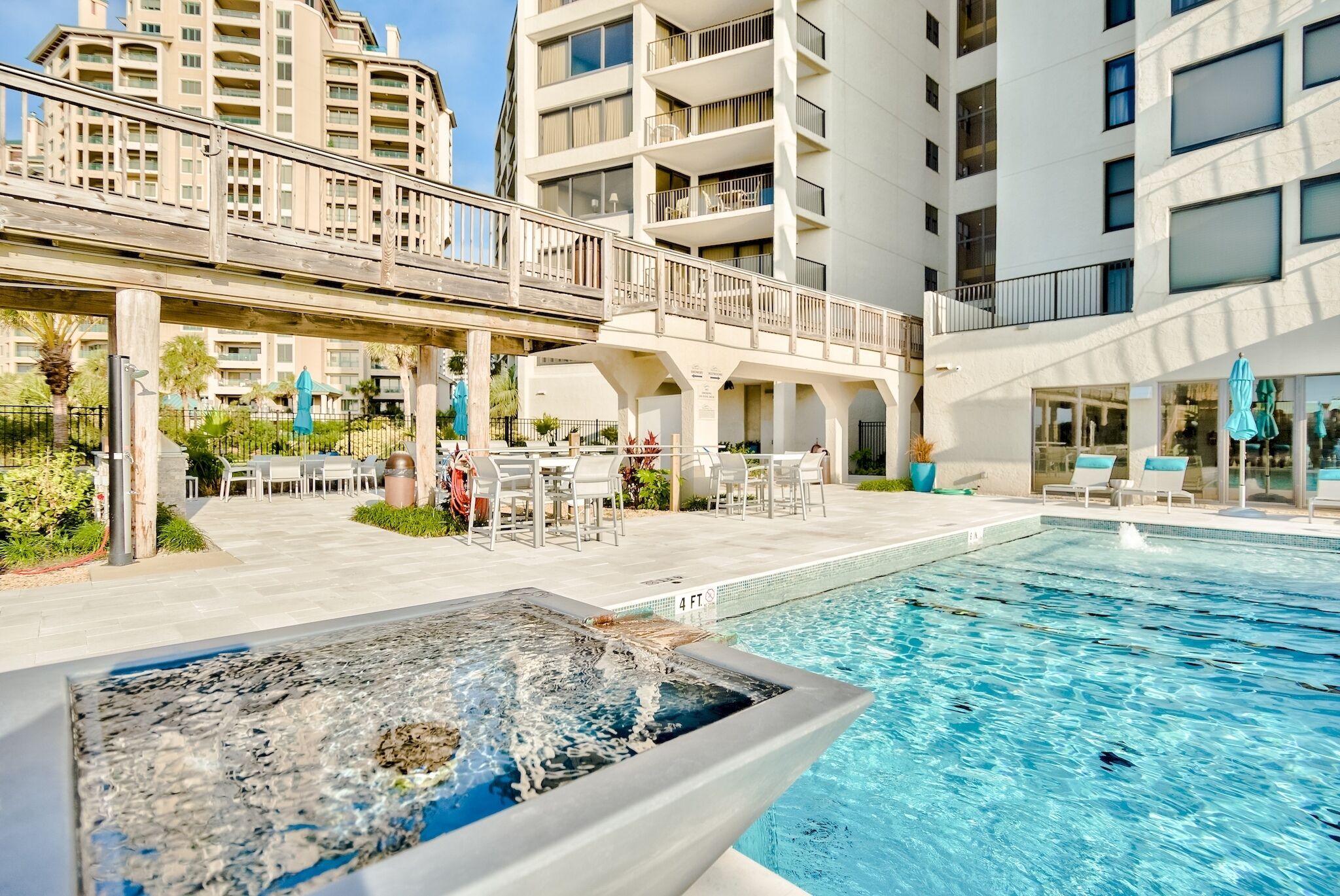 A hotel pool area with a hot tub, outdoor seating, and a covered patio.